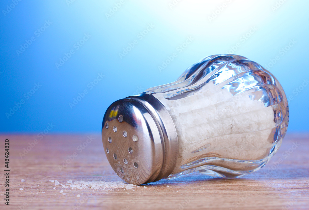 Glass saltcellar with salt on wooden table on blue background