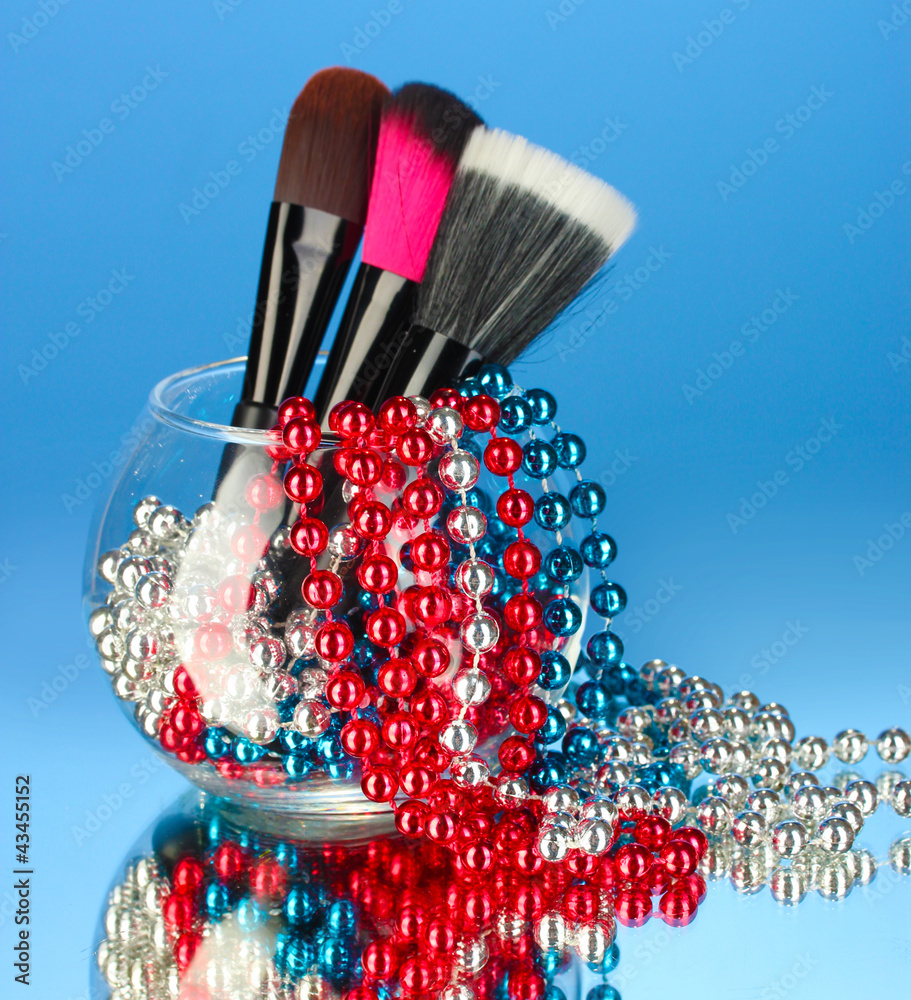 Make-up brushes in a bowl with pearl necklace on blue