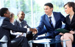 © ASDF - Two business man shaking hands with his team in office
