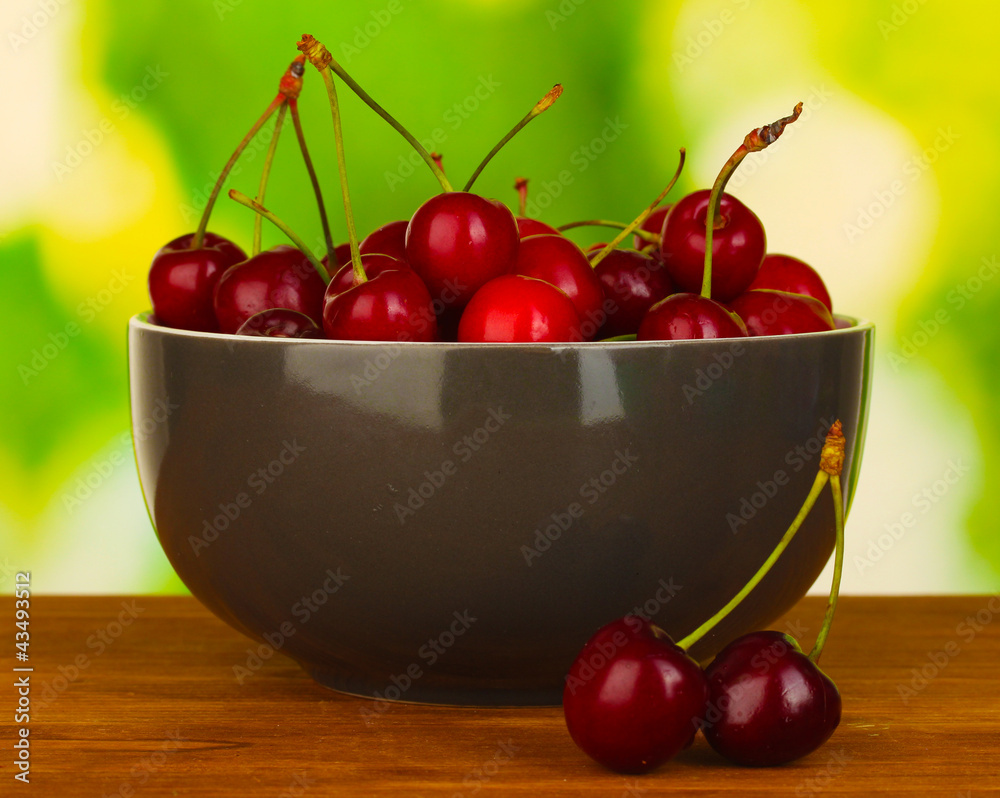 cherry in grey bowl on wooden table on green background