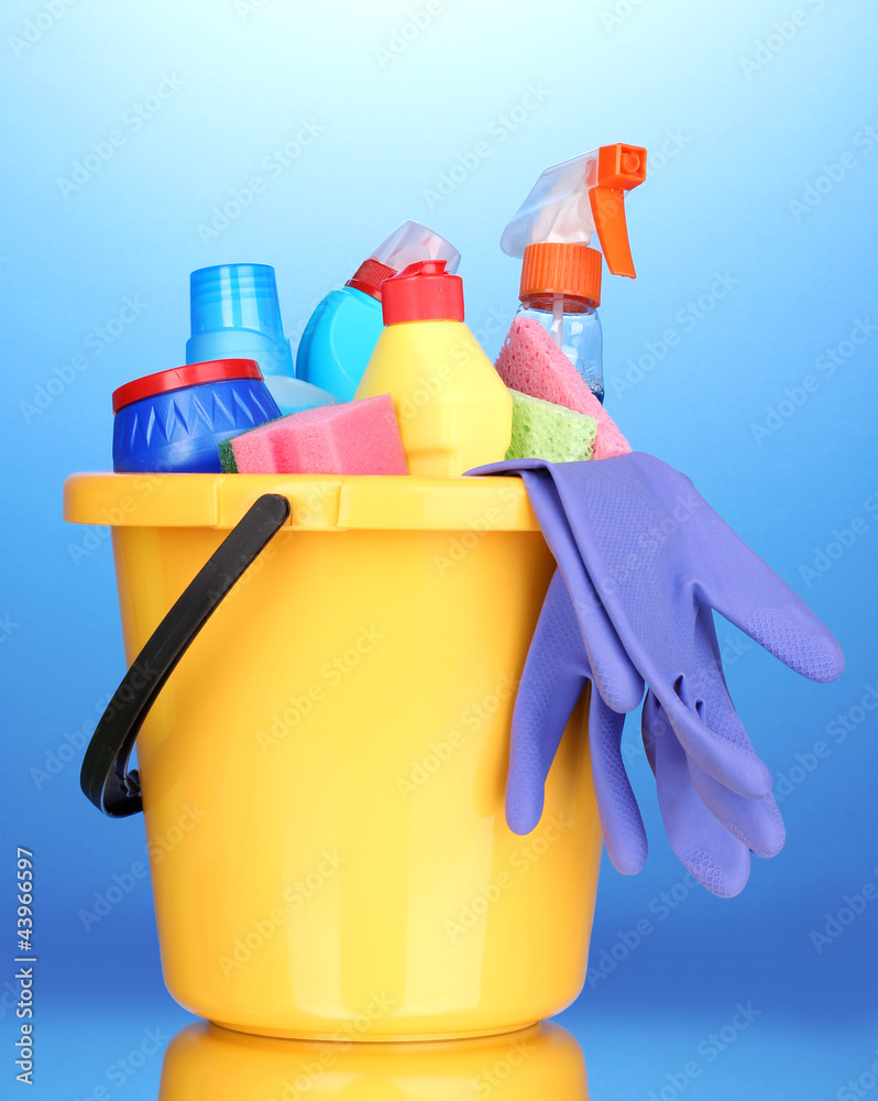 Bucket with cleaning items on blue background