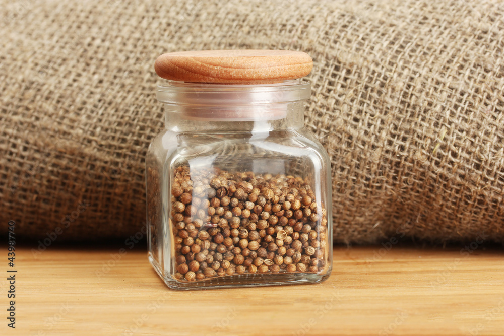 Jar of coriander seeds on canvas background close-up