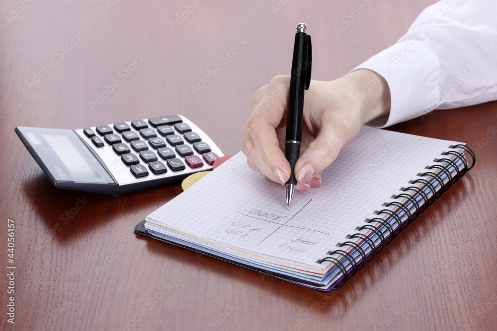 women hands with pencil, notebook and Calculator on wooden