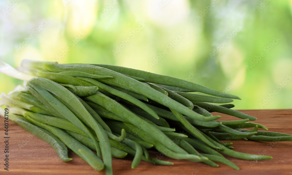 Green onion on a cutting board with knife on green background
