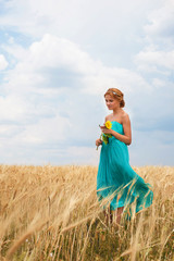 Pretty girl with sunflower walking through the wheat field