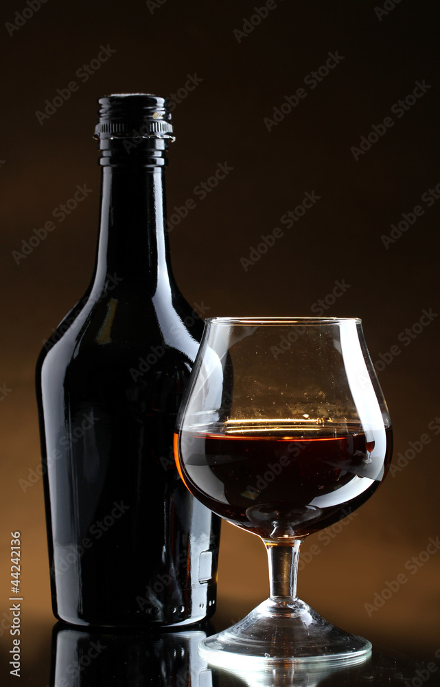 Glass of brandy and bottle on brown background