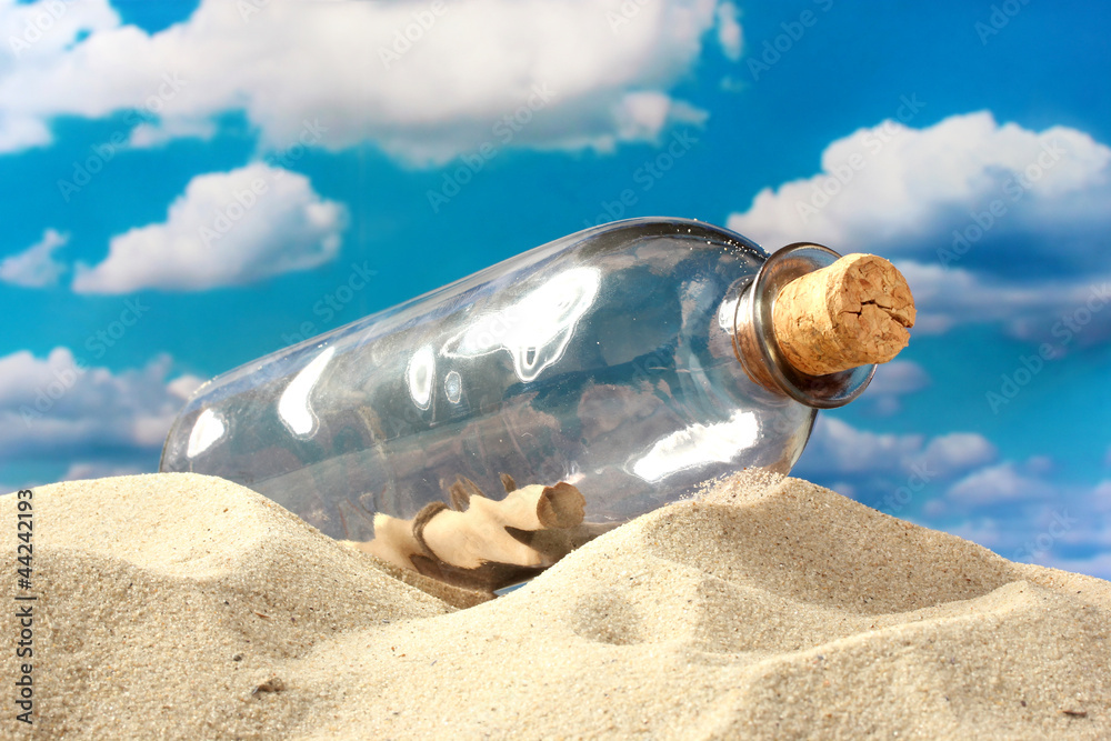 Glass bottle with note inside on sand, on blue sky background