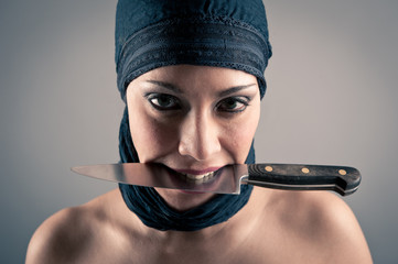 Veiled woman holding a knife against dark background. Intense po