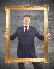 Portrait Of Businessman Holding A Golden Frame On Cement Backgro