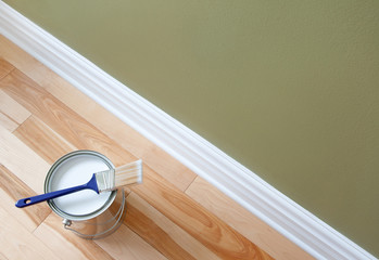 Paintbrush and an open can of white paint on wooden floor