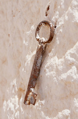 Close-up view of a rusty key on a rustic white stone wall