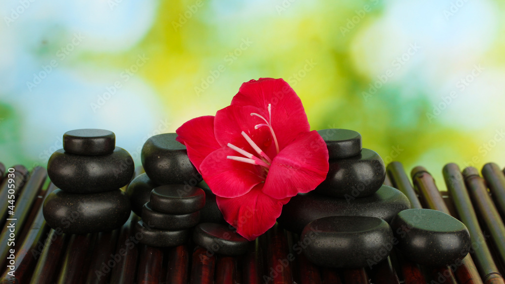 Spa stones with gladiolus bud on bamboo mat close-up