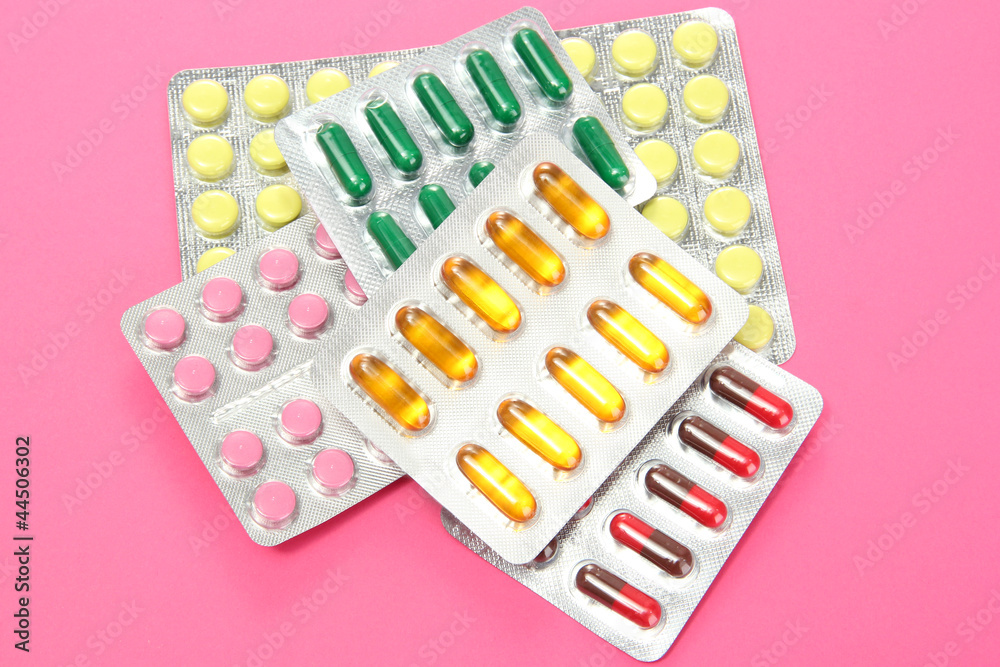 Capsules and pills packed in blisters, on pink background