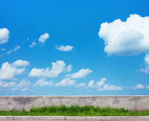 green grass, blue sky and concrete wall background