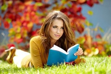 Poster - Young nice attentive woman lies on green grass and reads book ag