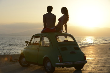 couple at sundown on the beach with car