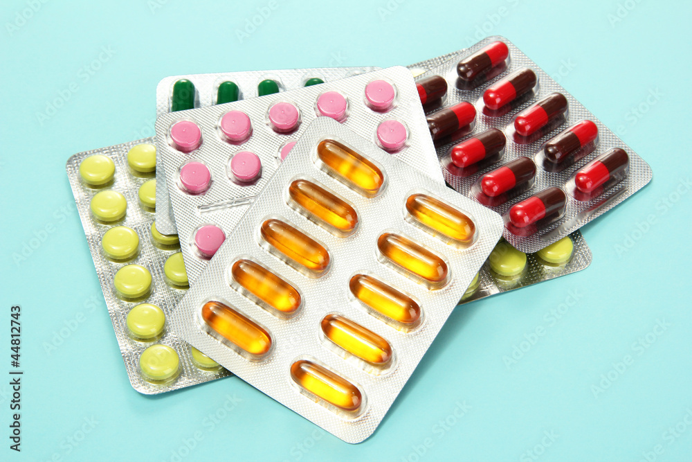 Capsules and pills packed in blisters, on blue background