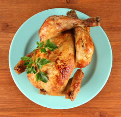 Roasted whole chicken on a blue plate on wooden background