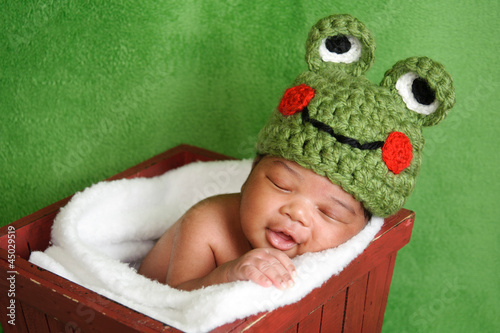 Naklejka na szybę Smiling newborn baby boy wearing a green crocheted frog hat