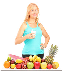 Wall Mural - Woman holding a glass of milk with pile of fruits on a table