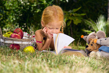 девочка читает книгу с игрушками на природе