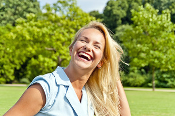 Beautiful young woman on green loawn in park playing her hair an