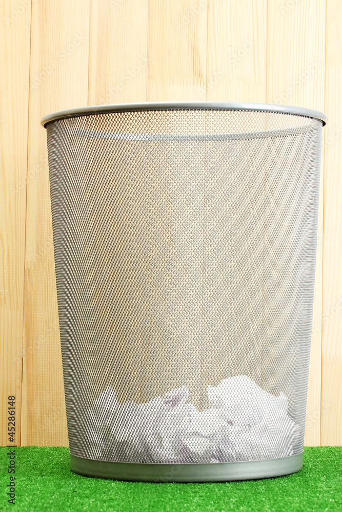 metal trash bin from paper on grass on wooden background