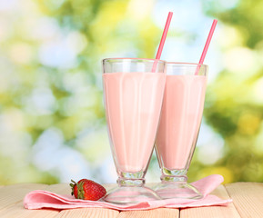 Wall Mural - Strawberry milk shakes on wooden table on bright background