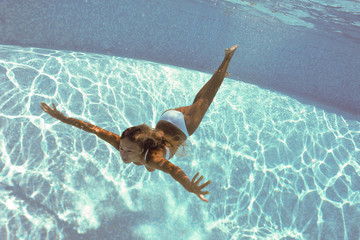 Underwater woman portrait with white bikini in swimming pool.