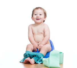 smiling baby boy sitting on chamber pot with toilet paper roll