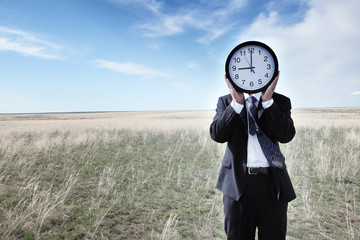 Portrait of a businessman holding a clock on grassland