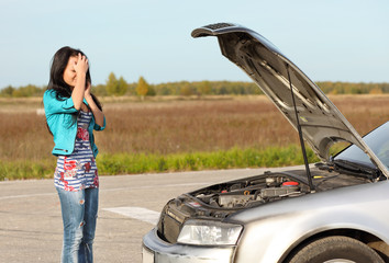 attractive brunette in front of her car broken