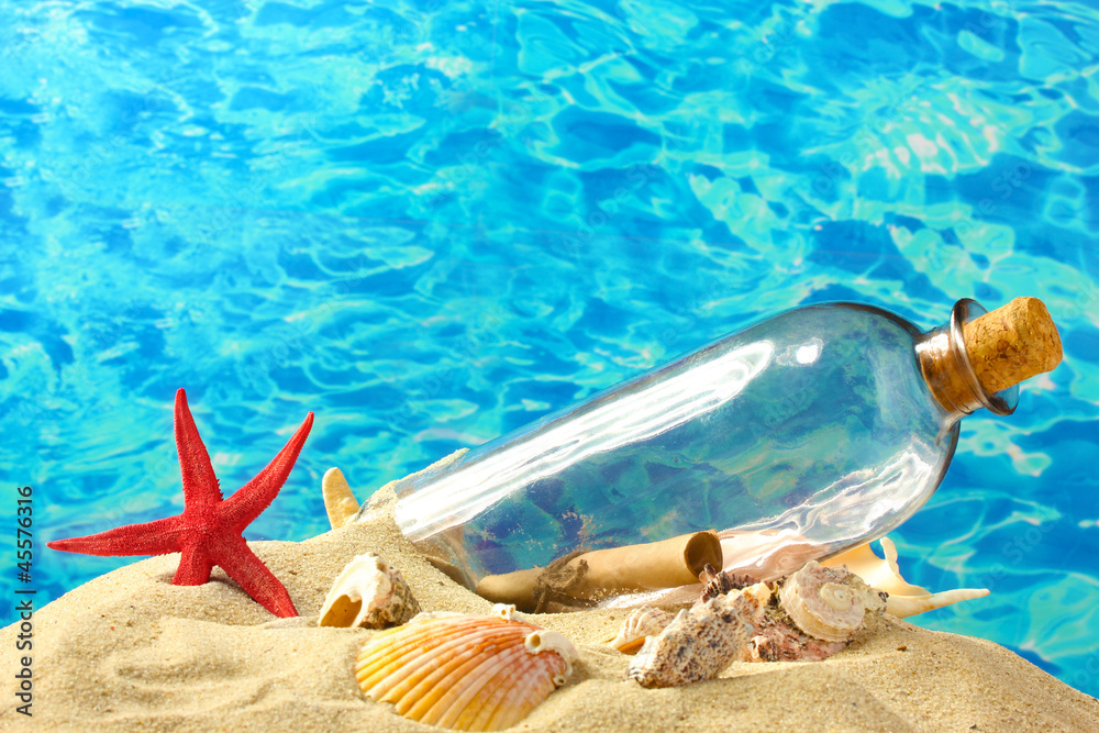 Glass bottle with note inside on sand, on blue sea background