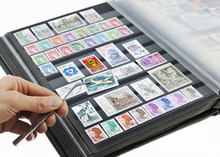Hand Holding Postage Stamp With Tweezers Over Album