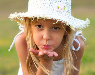 Cute little girl on the meadow blowing a kiss toward you