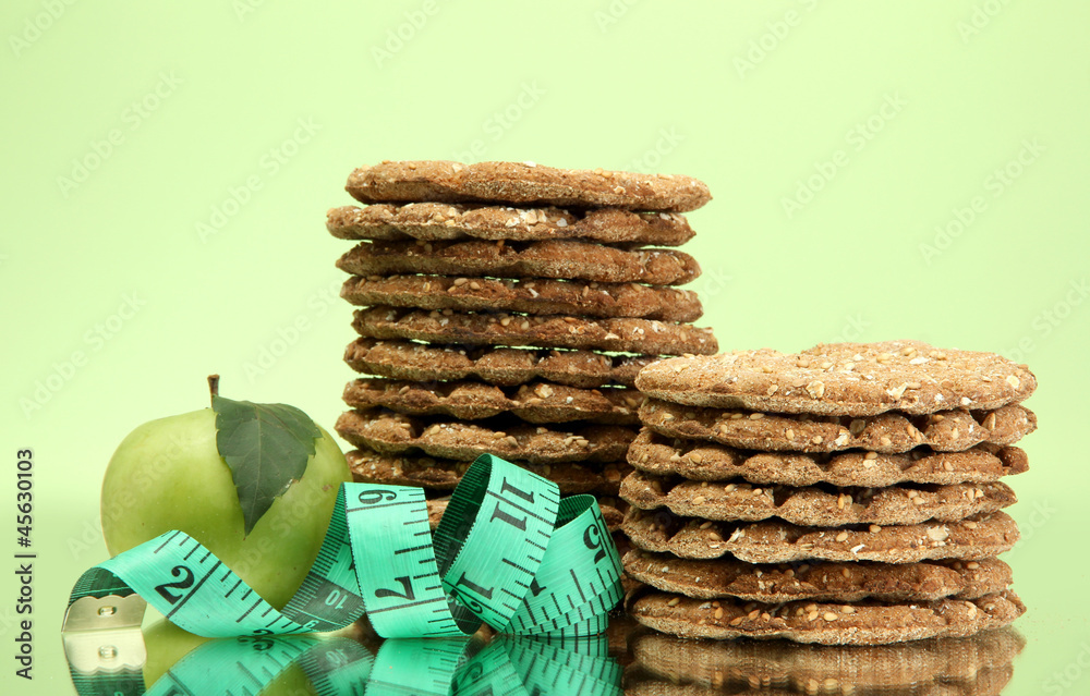 tasty crispbread, apple and measuring tape, on green background