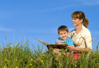 Woman, reading a book to the young boy in a green  meadow