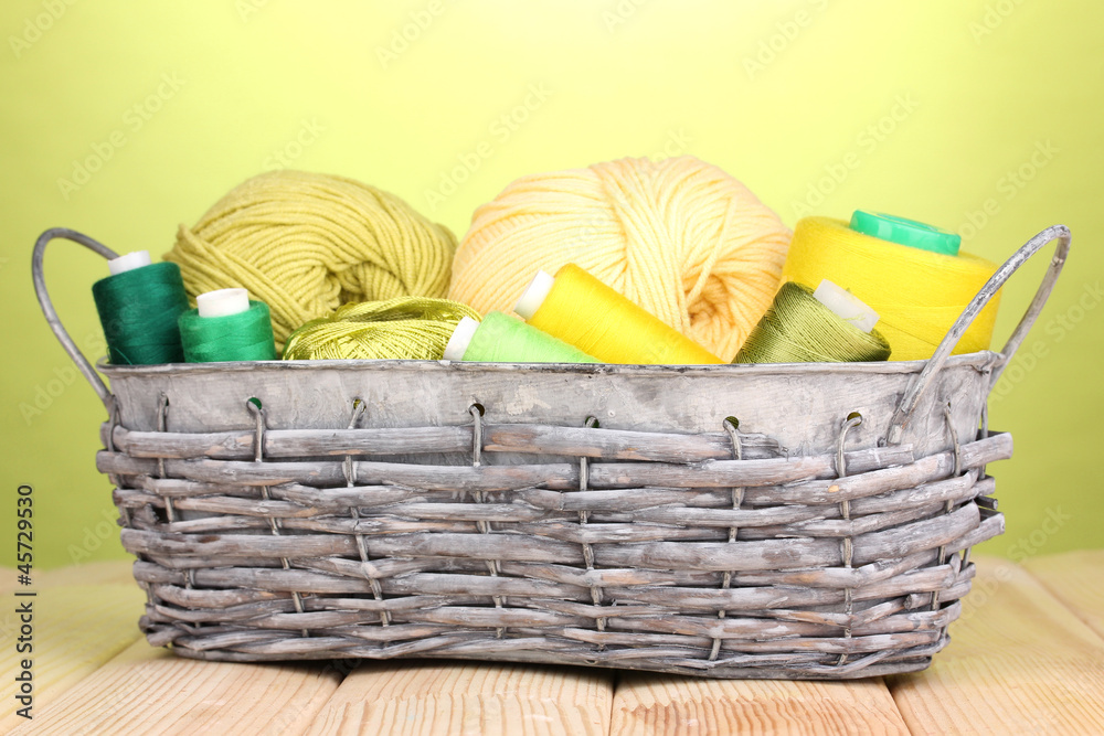 Bright threads in basket on wooden table on green background