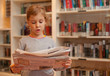 © Pavel Losevsky - Little girl stands against bookshelves read newspaper