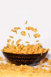 Golden cornflakes falling into black bowl - isolated on white