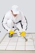 Worker removes old white tiles from floor with hammer