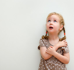 Portrait of little girl standing against the wall and looking up