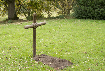 Single mock grave with wooden cross in grass field