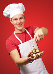 portrait of young cook man pressing a golden bell over red backg