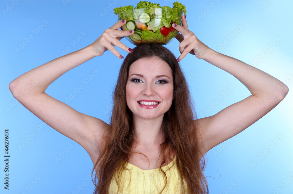 Beautiful woman with vegetable salad on blue background