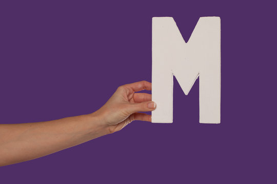 Female hand holding up the letter M from the left
