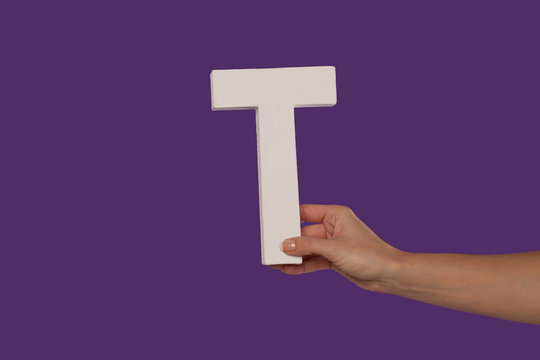 Female hand holding up the letter T from the right