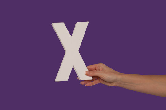 Female hand holding up the letter X from the right