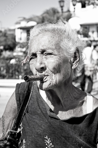 Fototapeta na wymiar Old wrinkled woman with red flower smoking cigar. Cuba