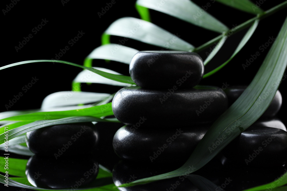Spa stones and green palm leaf on black background